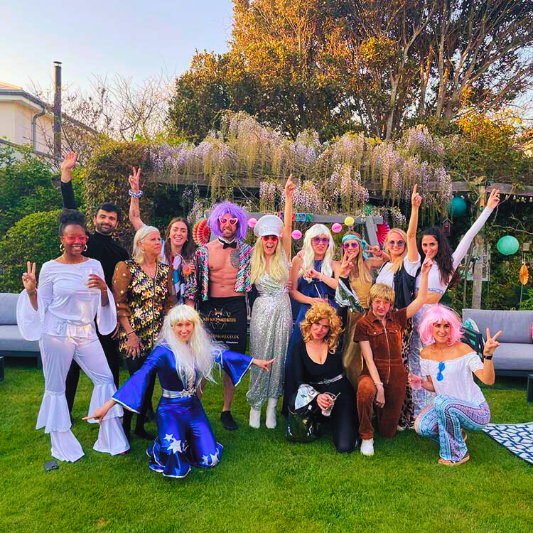 Butlers in the buff wearing green wigs and posing with guests in fancy dress outfits at a gay hen do.