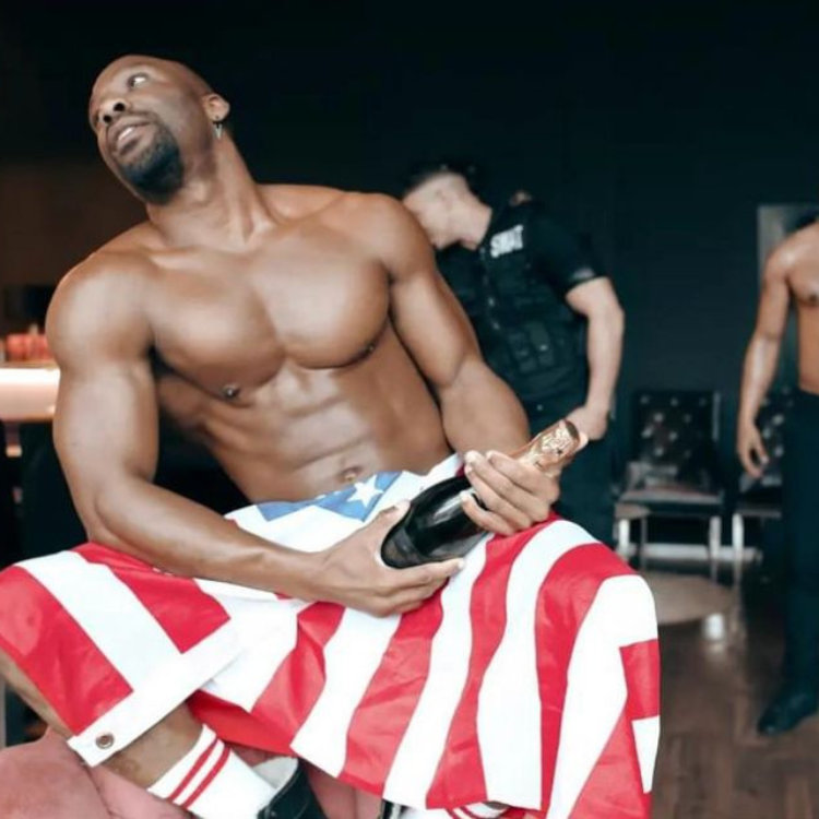 Male stripper in Byfleet holding a Union Jack flag and a bottle of champagne during a performance. Byfleet Male Strippers near me