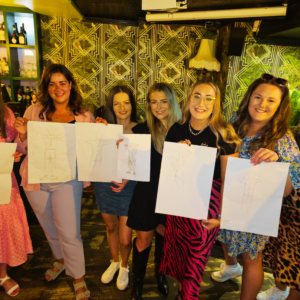 Guests at a Hen Party Life Drawing class holding their sketch boards, showcasing their artwork. Hen Party Life Drawing Sessions