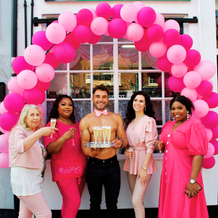 Naked butlers in pink bowties and jeans holding a wine tray and posing with guests at a cancer charity event in Manchester. Naked Butlers For Charity Events