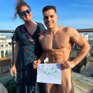 The bride-to-be, wearing a sash, and a model holding up a drawing at a Hen Party Life Drawing class. Hen Party Life Drawing Sessions