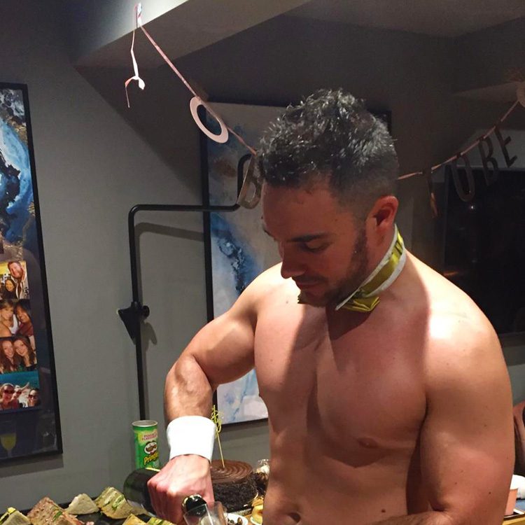 A naked butler holding a bottle of prosecco and serving drinks
