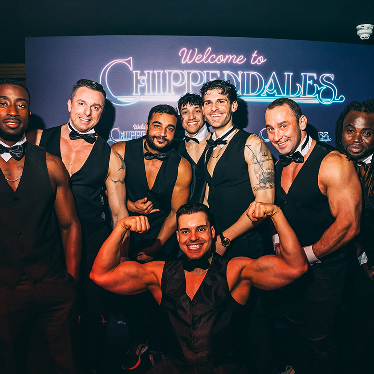 Eight butlers in the buff in Camden with collars, cuffs, and bow-ties posing with guests at a gala night event in Camden