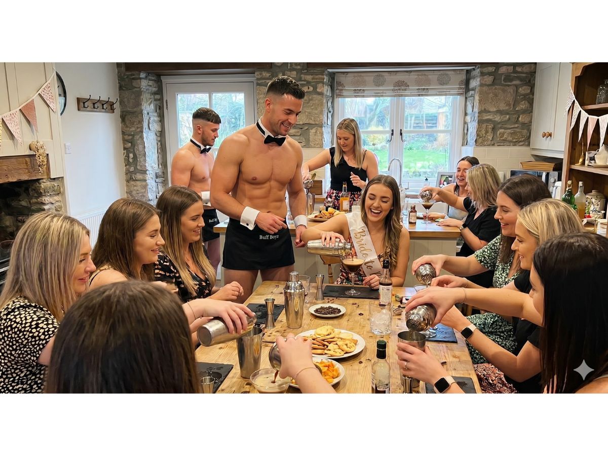 A group of cheerful women at a hen party participate in a cocktail-making masterclass with butlers in the buff. A woman in a 'Bride to Be' sash pours a drink, surrounded by friends shaking cocktail tins and smiling